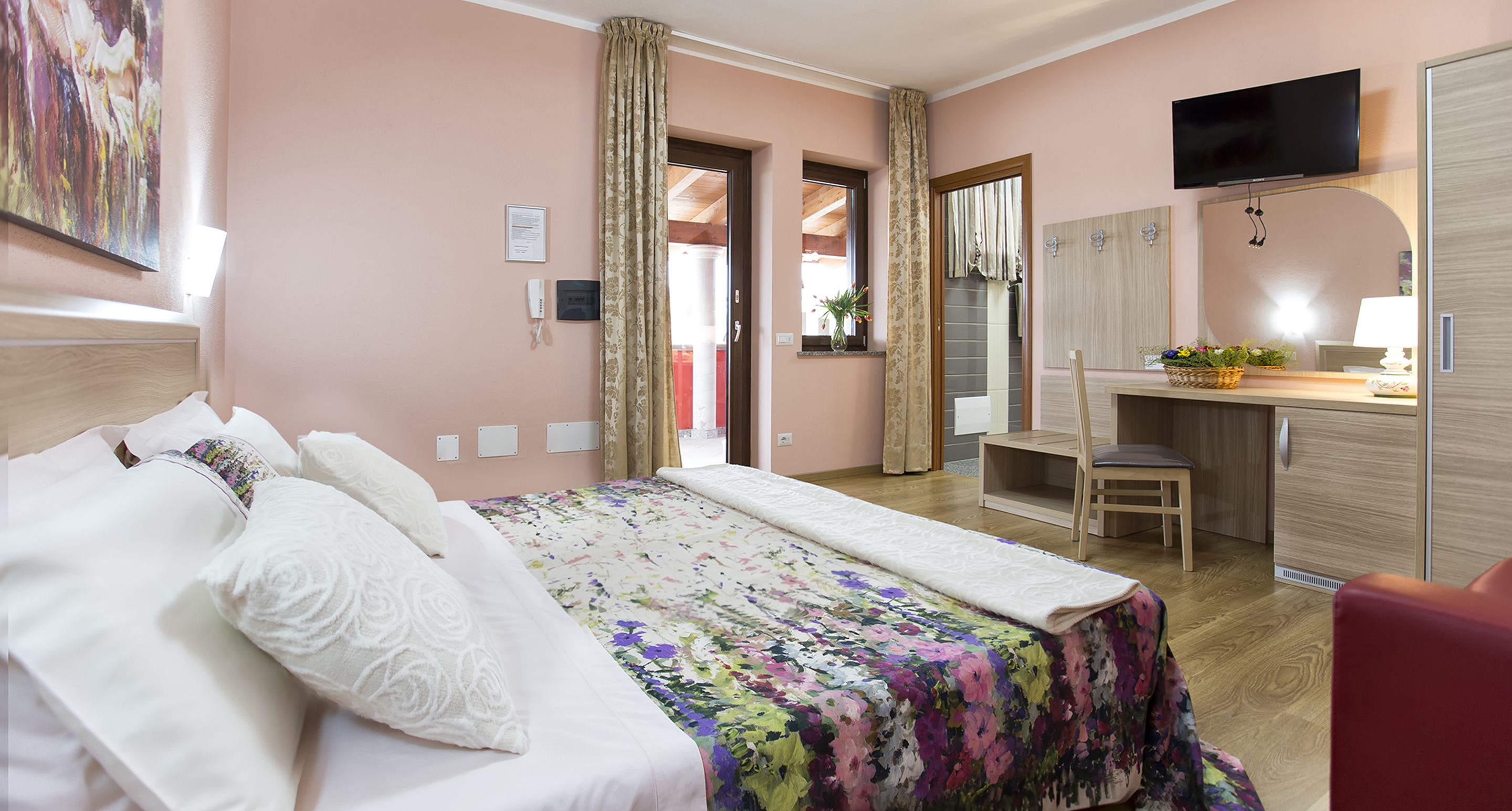 A hotel room with a bed, a desk, a chair, a TV, and a bathroom visible through an open door.