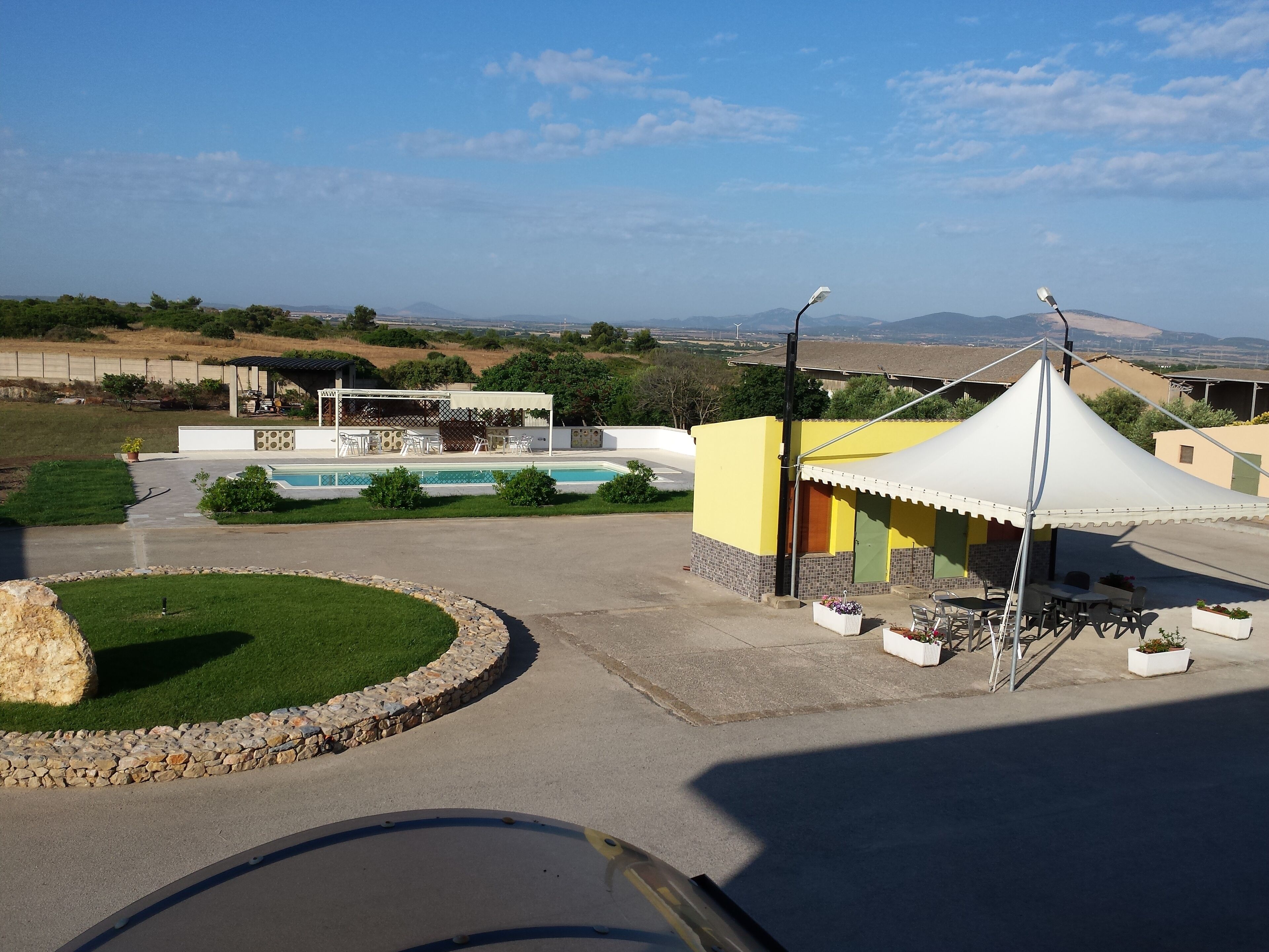 A pool area with a covered seating area, a stone border, and a view of distant hills.