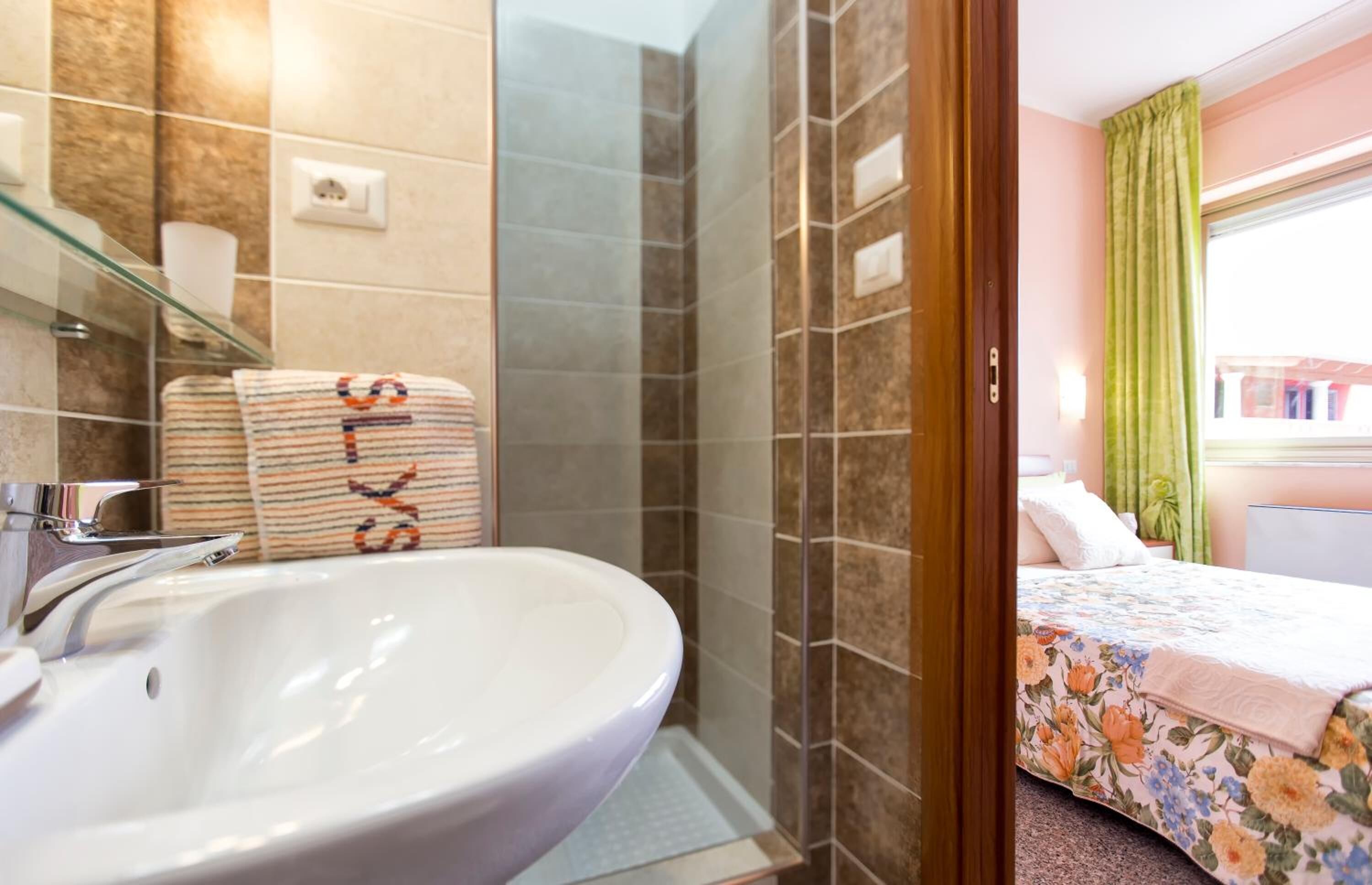 Un baño con un lavamanos grande, cabina de ducha de vidrio y una cama con ropa de cama floral.