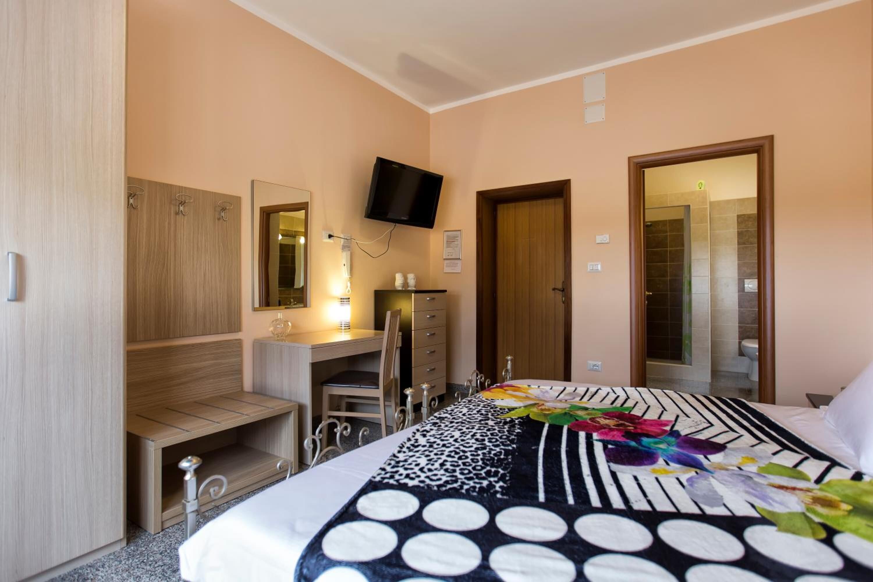 A hotel room with a bed, a desk, a chair, a wardrobe, and a television.