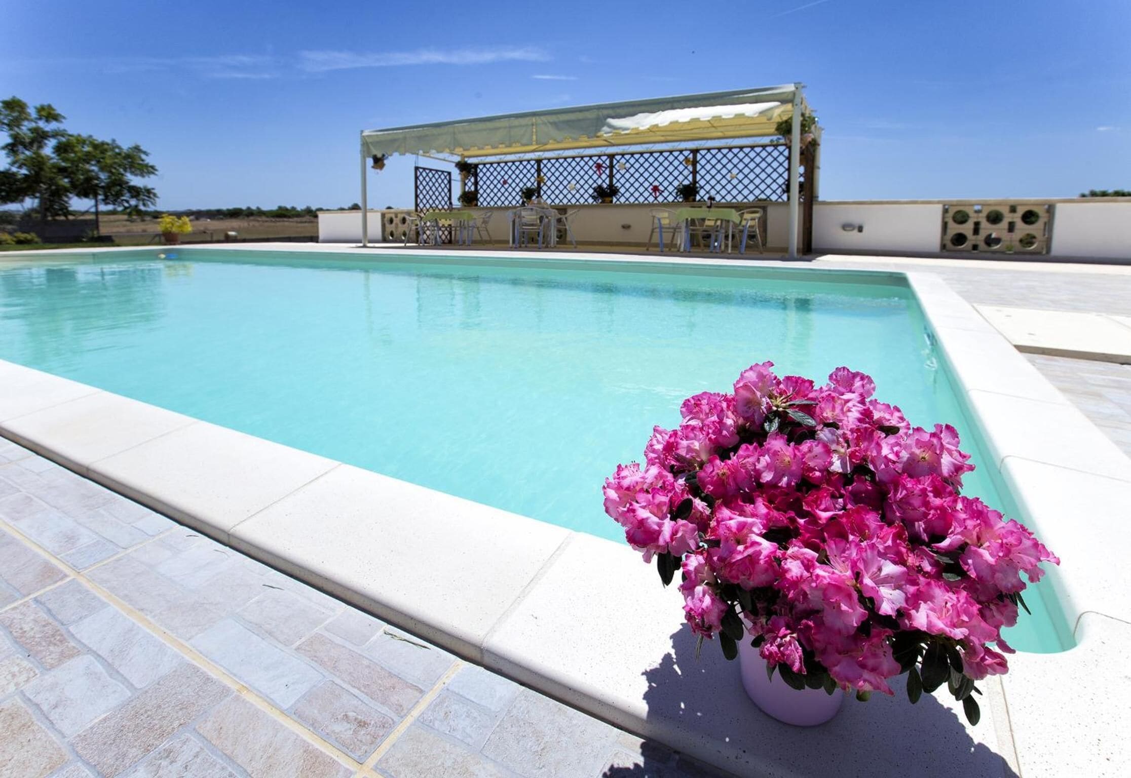 Una piscina con una pérgola y sillas, rodeada por un patio empedrado.