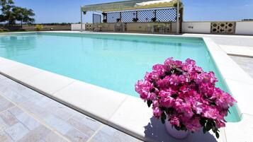 Una piscina con una pérgola y sillas, rodeada por un patio empedrado.