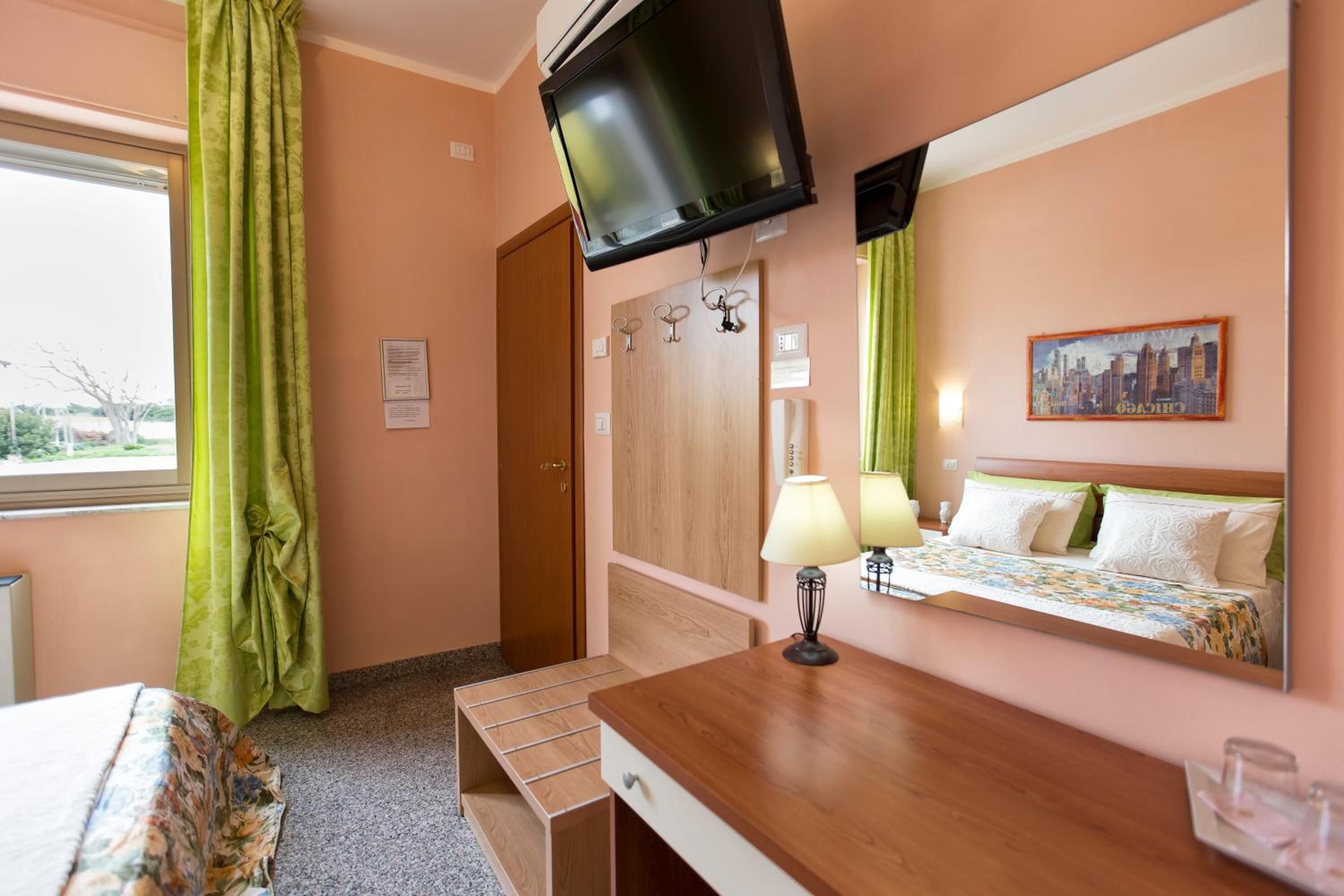 A hotel room with a bed, a desk, a television mounted on the wall, and a window with curtains.