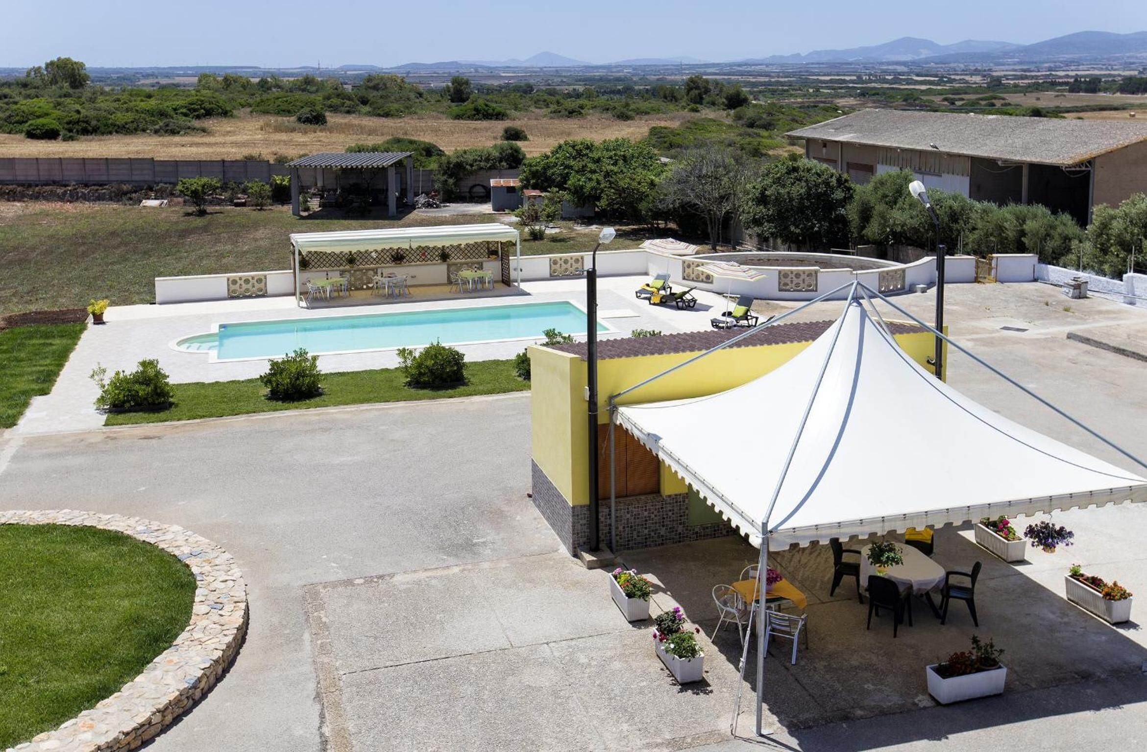 A pool area with a covered patio, outdoor seating, and a view of the surrounding landscape.