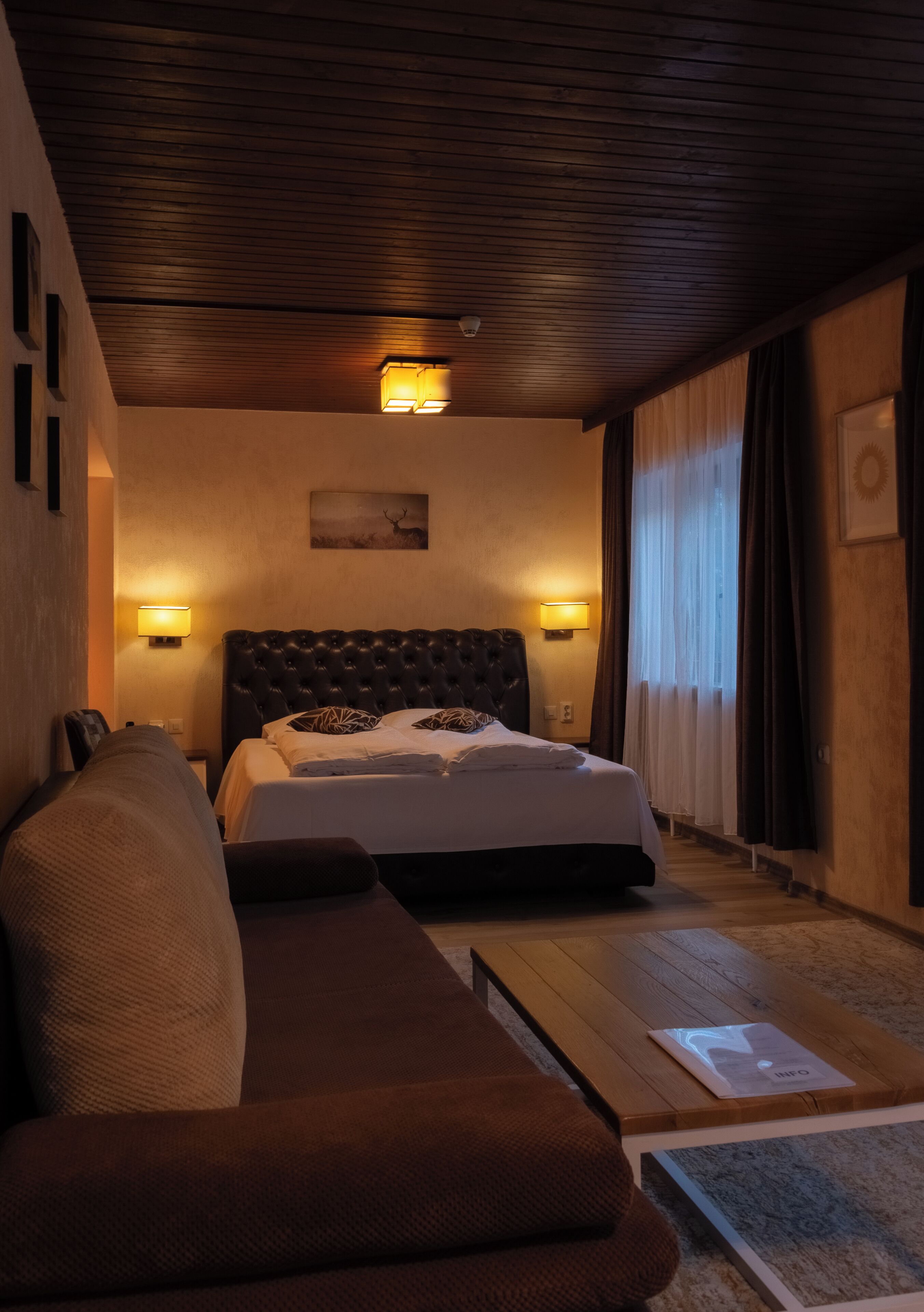 Een hotelkamer met een groot bed, een bank, twee wandlampen, een schilderij en een raam met gordijnen.