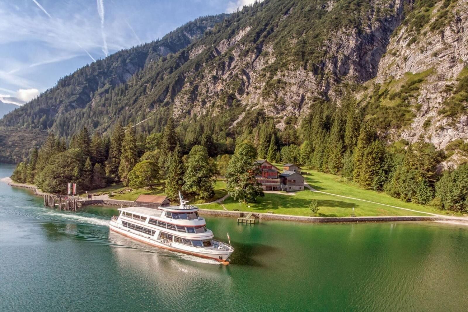 A riverboat docked at a lakeside property with a mountain backdrop.