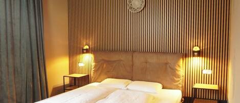 Un dormitorio con una cama grande, cabecera de listones de madera, dos mesitas de noche con lámparas y un banco al pie de la cama.