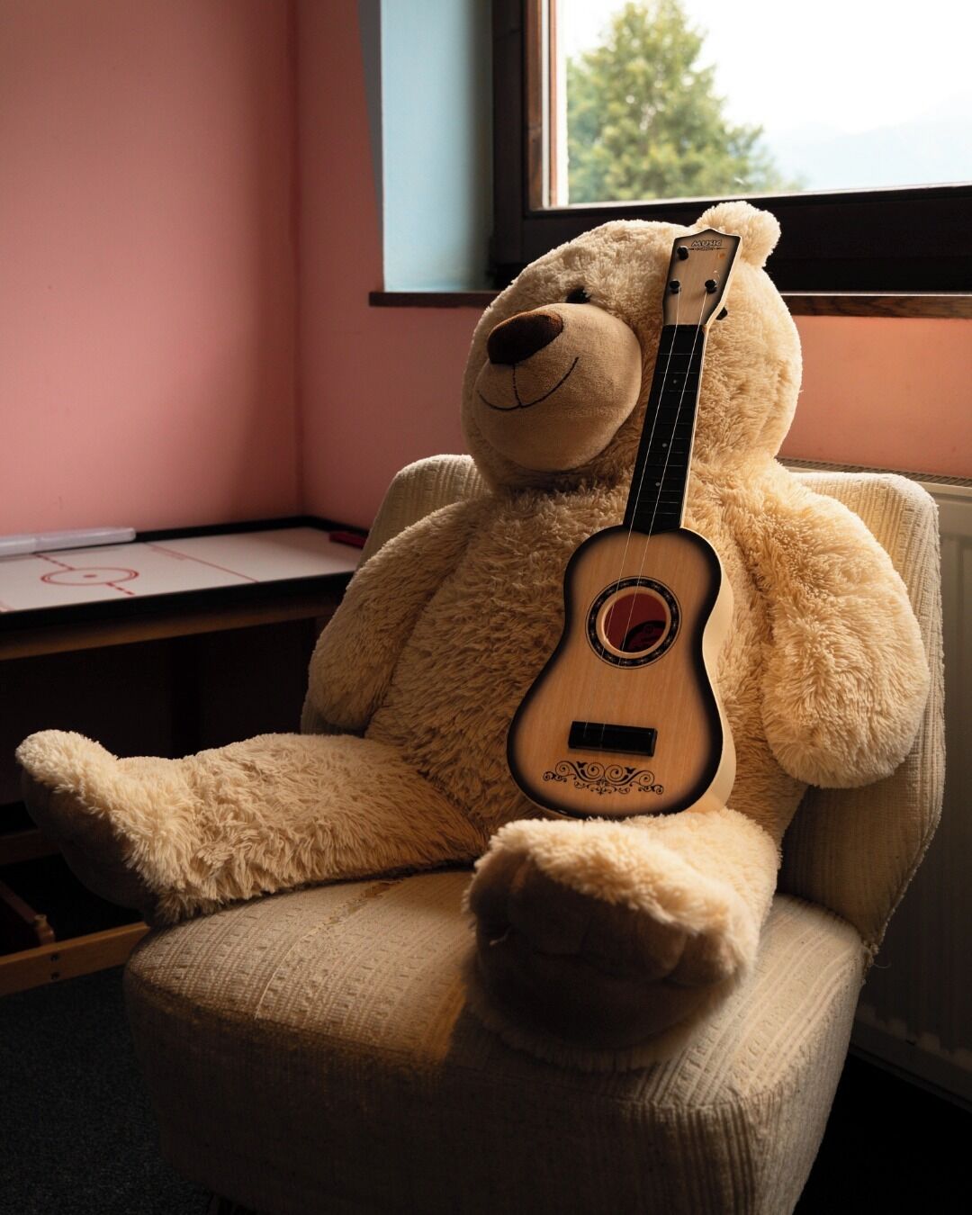 Un oso de peluche grande sentado en una silla con un ukelele.