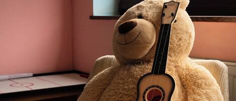 Un oso de peluche grande sentado en una silla con un ukelele.