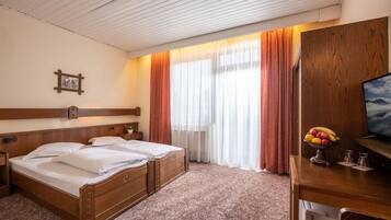 Une chambre d’hôtel avec un lit double, une tête de lit en bois, un bureau avec un panier de fruits et un téléviseur.