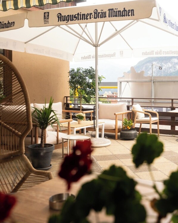 A rooftop terrace with outdoor seating, potted plants, and a view of the city.