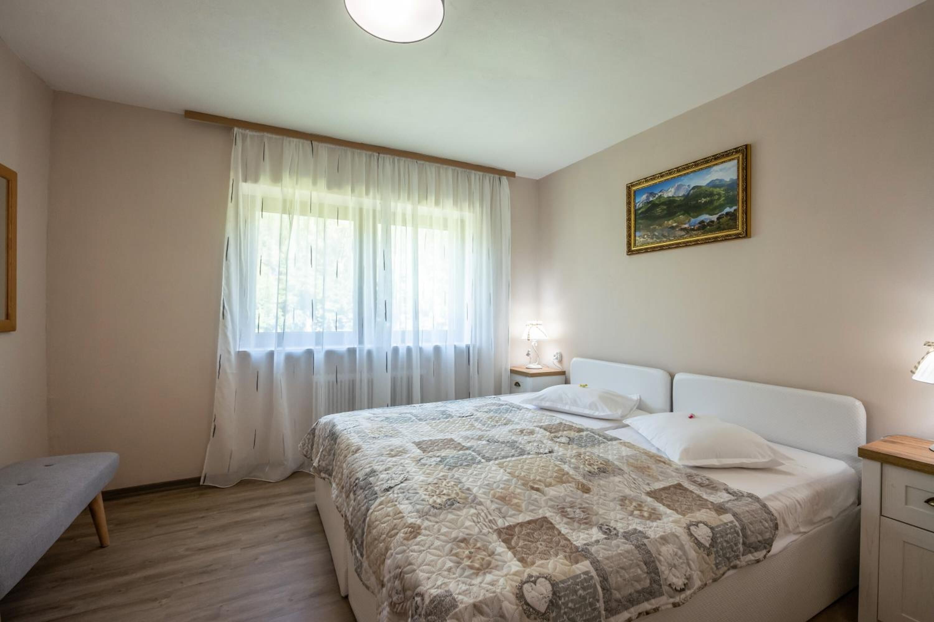 Une chambre à coucher avec un lit, une table de chevet, une lampe, un banc et un tableau accroché au mur.