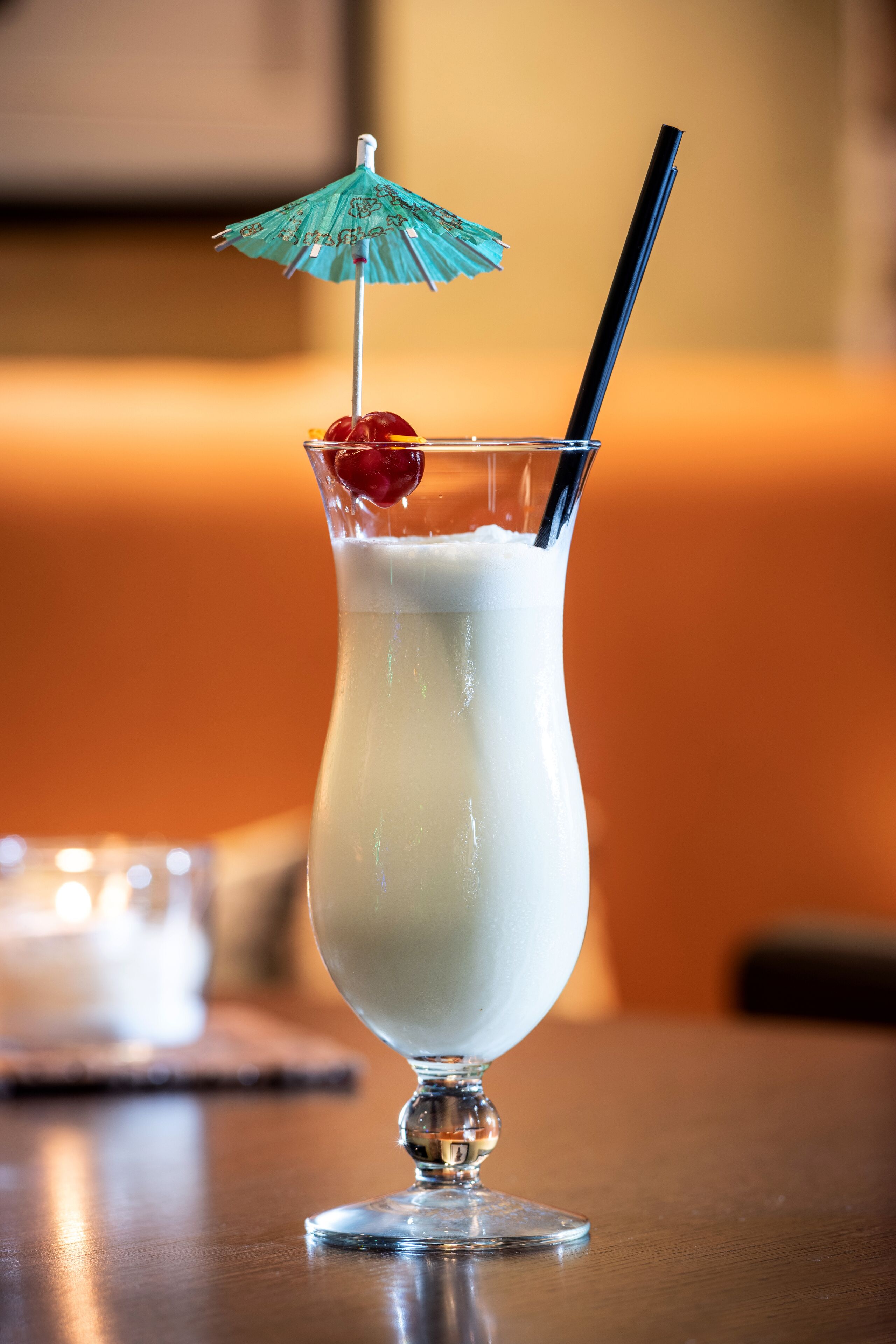 A tall glass with a straw, a cherry, and a blue umbrella on top, placed on a wooden table.