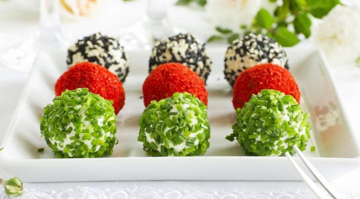 A white rectangular plate with six spherical food items, each with a different colored coating.