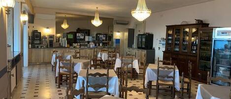 A restaurant with wooden tables and chairs, a bar area, and a chandelier.