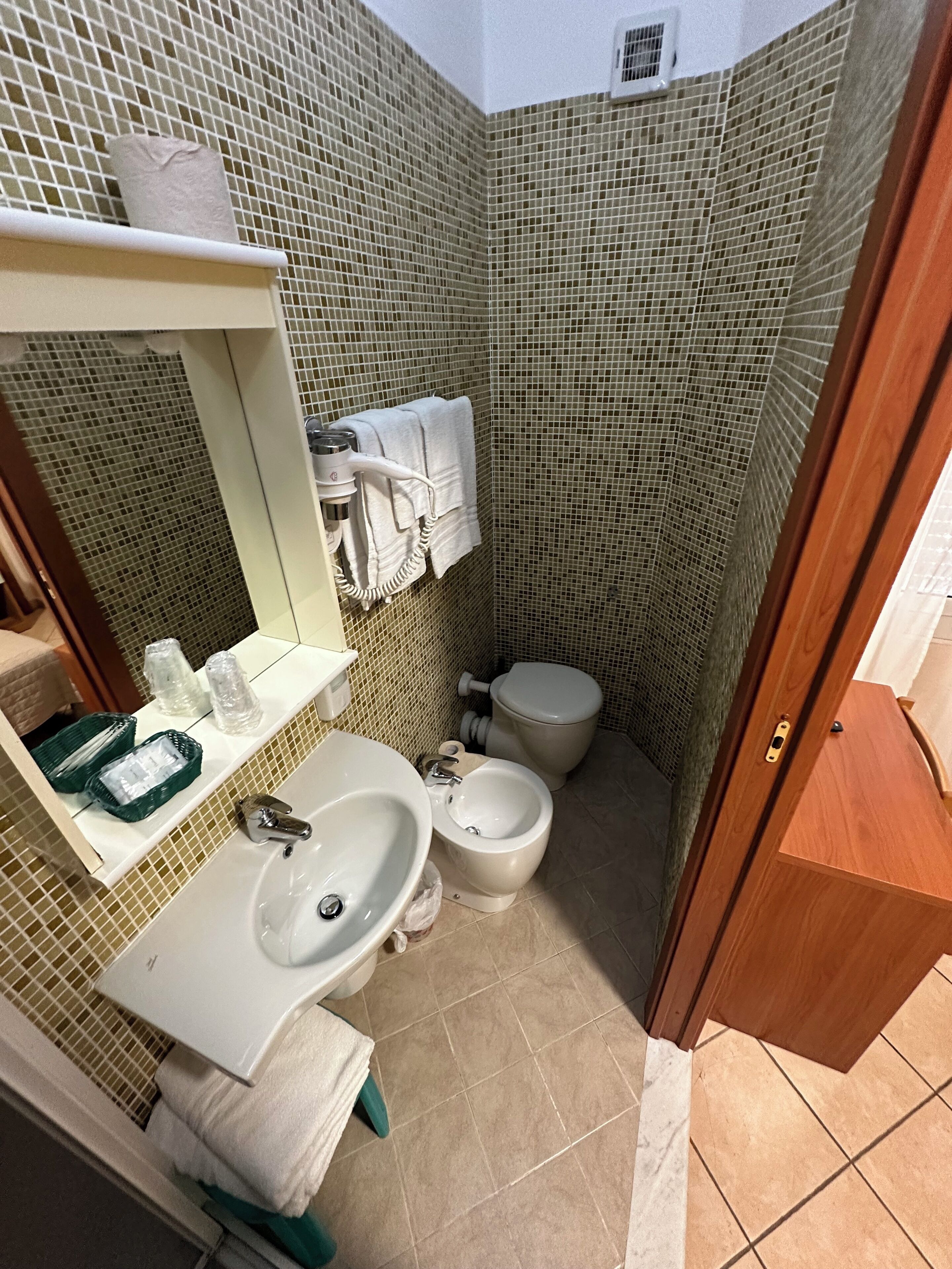 A small bathroom with a sink, mirror, and toilet. There are towels and toiletries on the counter.