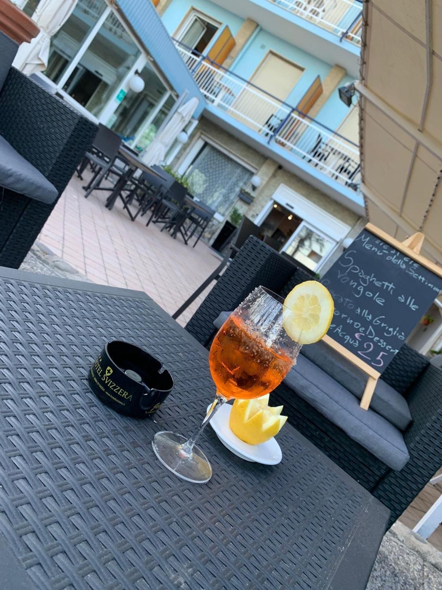 Ein Essbereich im Freien mit einem Tisch für zwei Personen, komplett mit einem Cocktailglas mit Zitronenscheibe und einem schwarzen Untersetzer mit Hotel-Logo.
