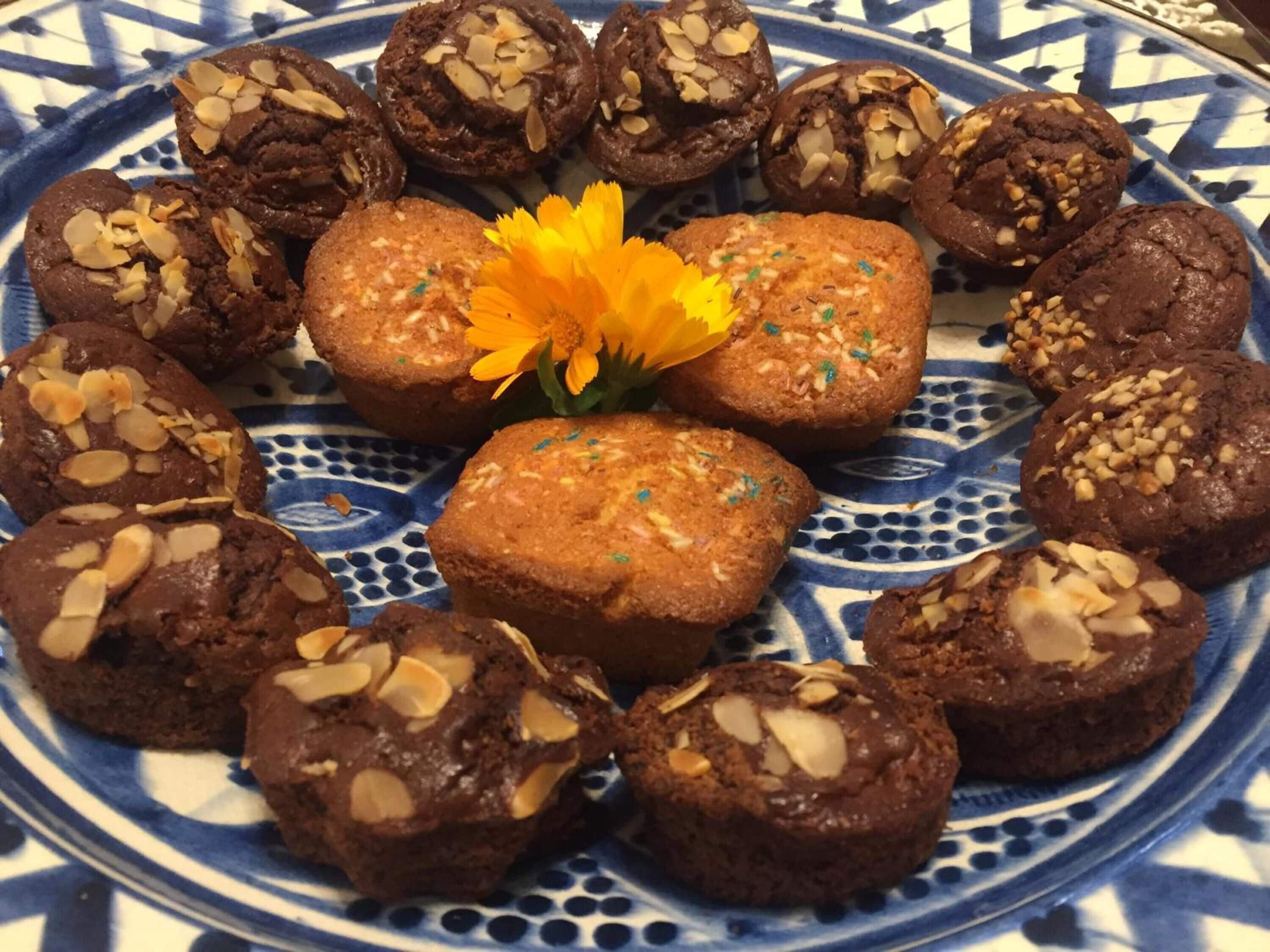 A plate of assorted muffins with almonds, a yellow flower, and a blue patterned plate.