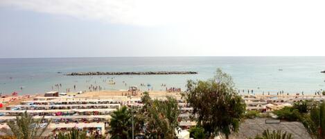A beach with numerous people, a pier, and several beachside stalls.