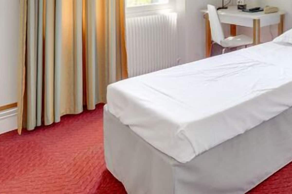 A hotel room with two single beds, a small bedside table, a chair, and a radiator.