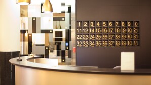 Un mostrador de recepción de hotel con una pantalla digital de números e iluminación colgante.