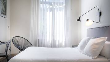 Una habitación de hotel con cama, escritorio, silla y lámpara de pared.