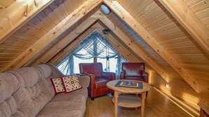 A cozy attic room with a wooden ceiling, a cushioned sofa, two leather chairs, and a small wooden table. - Gljúfurbústaðir (Sveitarfélagid Ölfus)