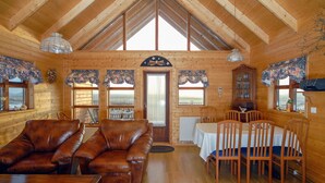 A wooden cabin interior with a dining area, leather sofa, and a view through the door. - Gljúfurbústaðir (Sveitarfélagid Ölfus)