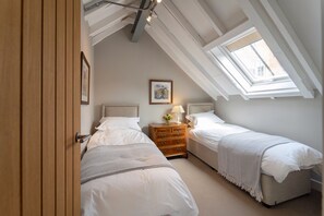 A bedroom with two beds, a wooden dresser, a lamp, and a framed picture on the wall.