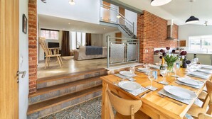 A dining area with a wooden table set for a meal, a staircase leading to an upper level, and a brick wall. - The Dairy, Freston, Suffolk (Freston)