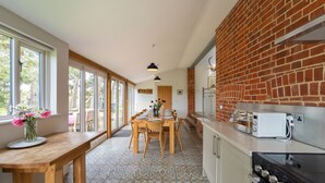 A modern kitchen with a brick wall, large windows, and a dining area with a wooden table and chairs. - The Dairy, Freston, Suffolk (Freston)