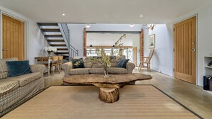 A modern living room with a large wooden coffee table, striped sofas, and a staircase. - The Dairy, Freston, Suffolk (Freston)