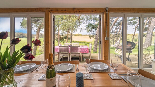 A dining table set for four with a bottle of champagne, glasses, and a vase of tulips. - The Dairy, Freston, Suffolk (Freston)