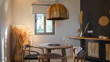 Een eethoek met een ronde houten tafel, twee stoelen, een hangende houten lamp, een grote geweven plant en een keukenblad met een geweven onderzetter.