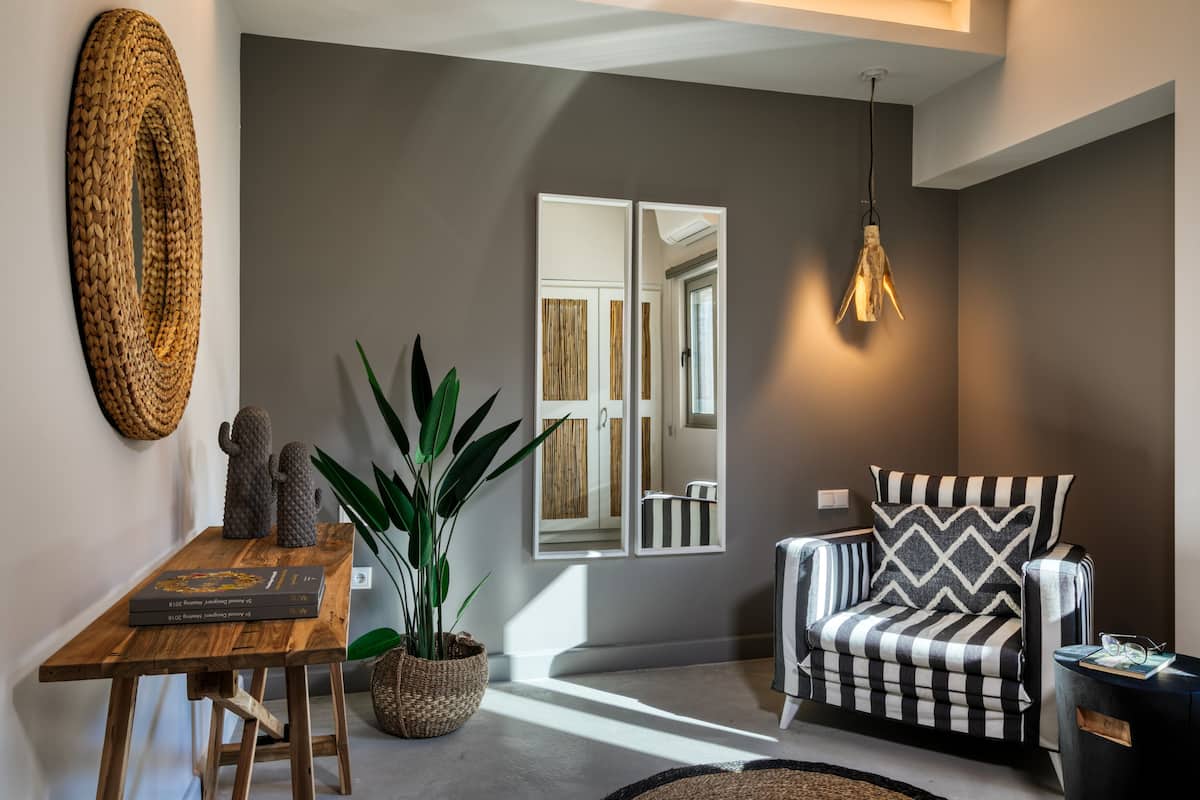 Un salón moderno con una mesa de centro de madera, una planta en maceta, un sillón a rayas y un espejo grande que refleja la habitación.