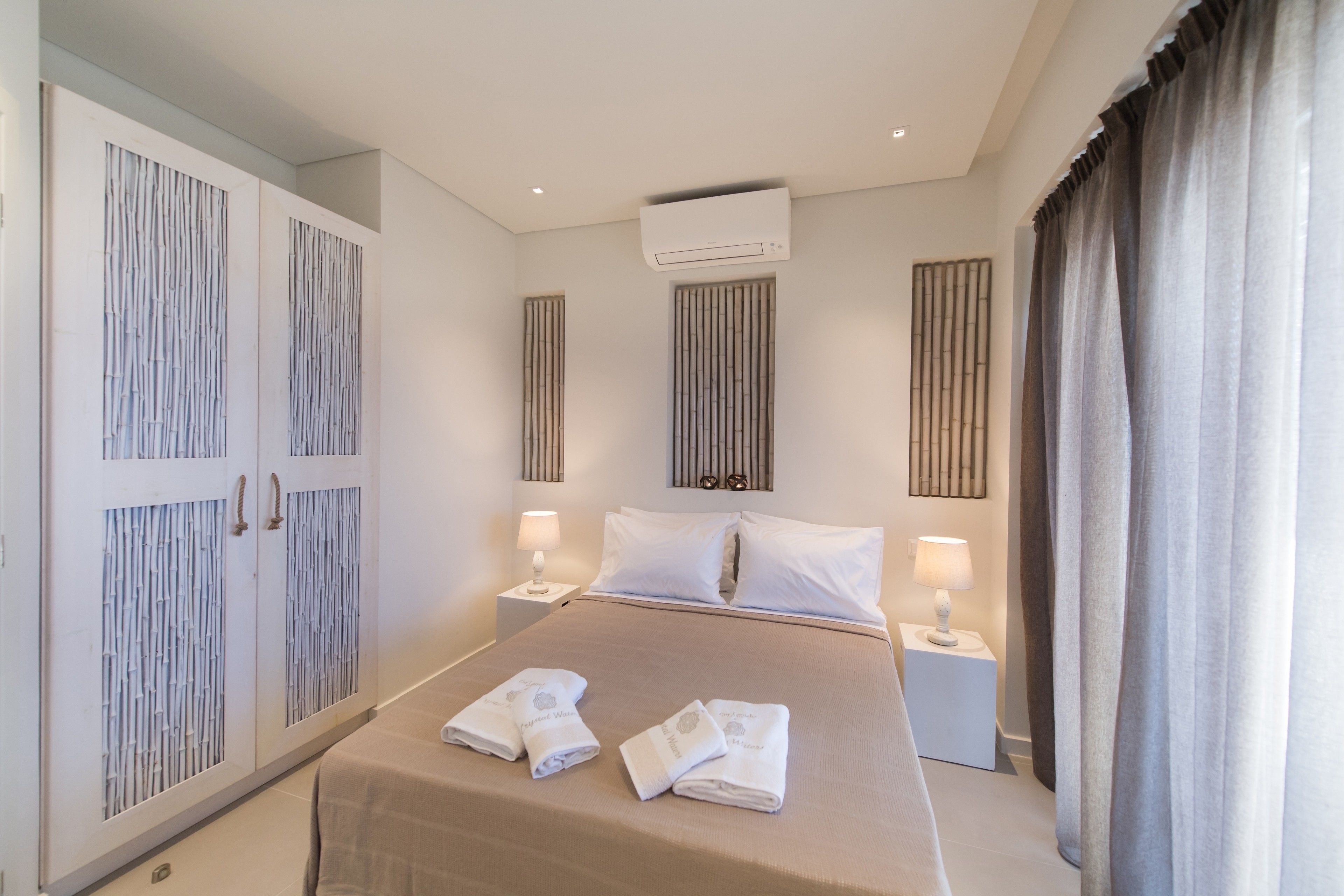 A hotel room with a bed, two bedside tables with lamps, a wardrobe, and an air conditioning unit.