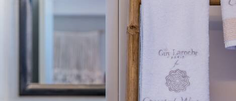 A bathroom with a white sink, a mirror, and a bamboo towel rack with towels labeled "Guy Laroche Paris" and "Crystal Water."