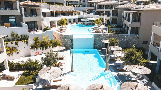 Un resort con una piscina central rodeada de áreas de descanso y sombrillas, con edificios de varios pisos al fondo.