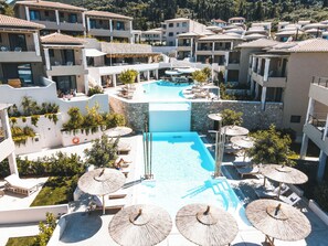 Un resort con una piscina central rodeada de áreas de descanso y sombrillas, con edificios de varios pisos al fondo.