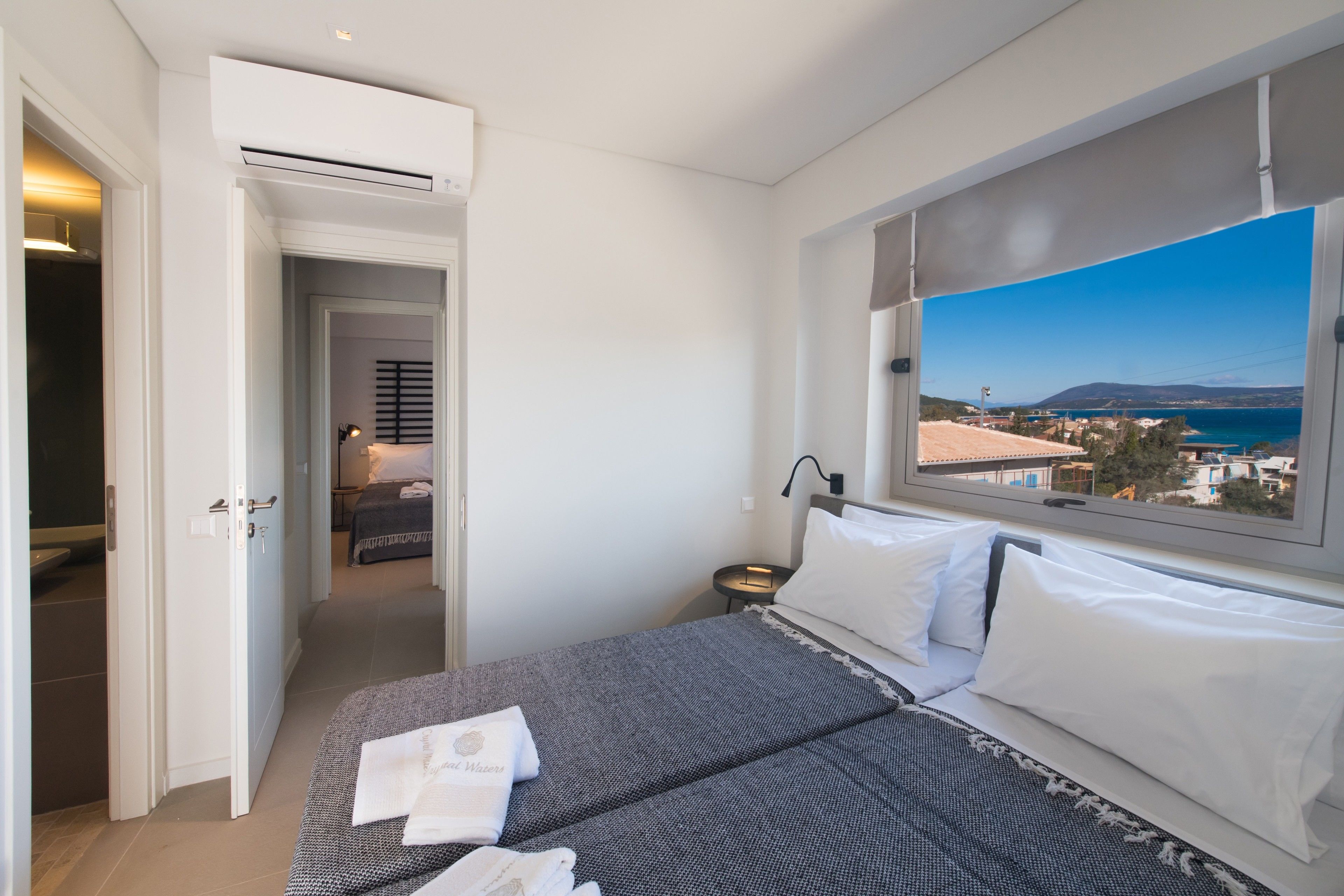 Una camera d'albergo con un letto, un comodino, una finestra vista mare e un condizionatore.
