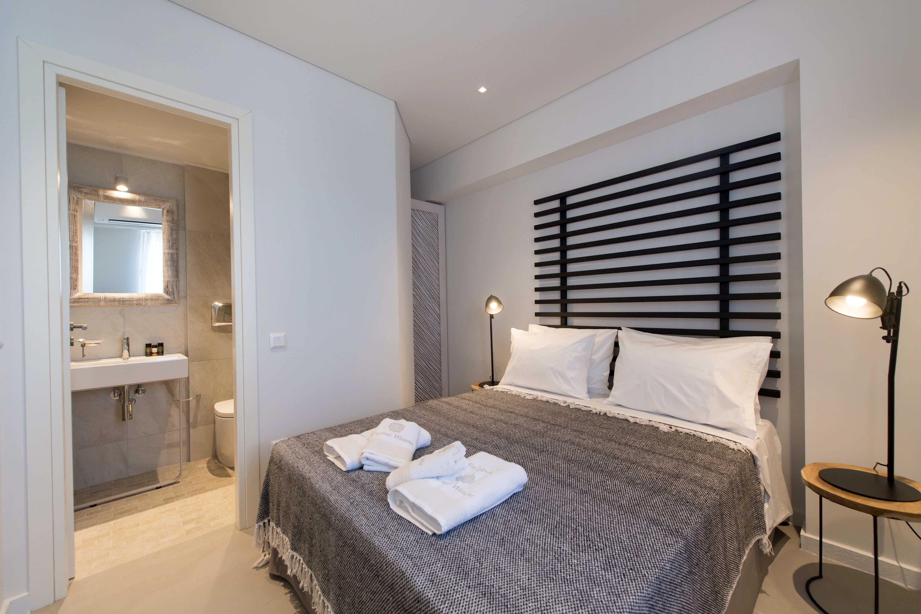 Un dormitorio moderno con una cama grande, lámparas de noche y un baño visible a través de una puerta abierta.