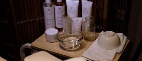 Zona de tratamientos de spa con una mesa de madera que sostiene varios productos para el cuidado de la piel, un tazón de vidrio y una toalla con el texto "Central Waves".