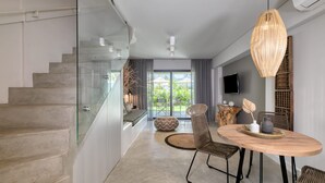 Un interior moderno con una escalera, una zona de comedor con una mesa redonda, sillas de mimbre y una gran lámpara de fibra.