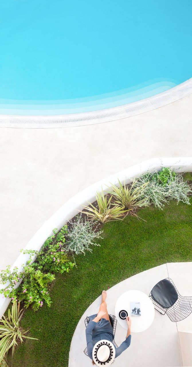 A person relaxing on a circular outdoor seating area with a pool in the background.