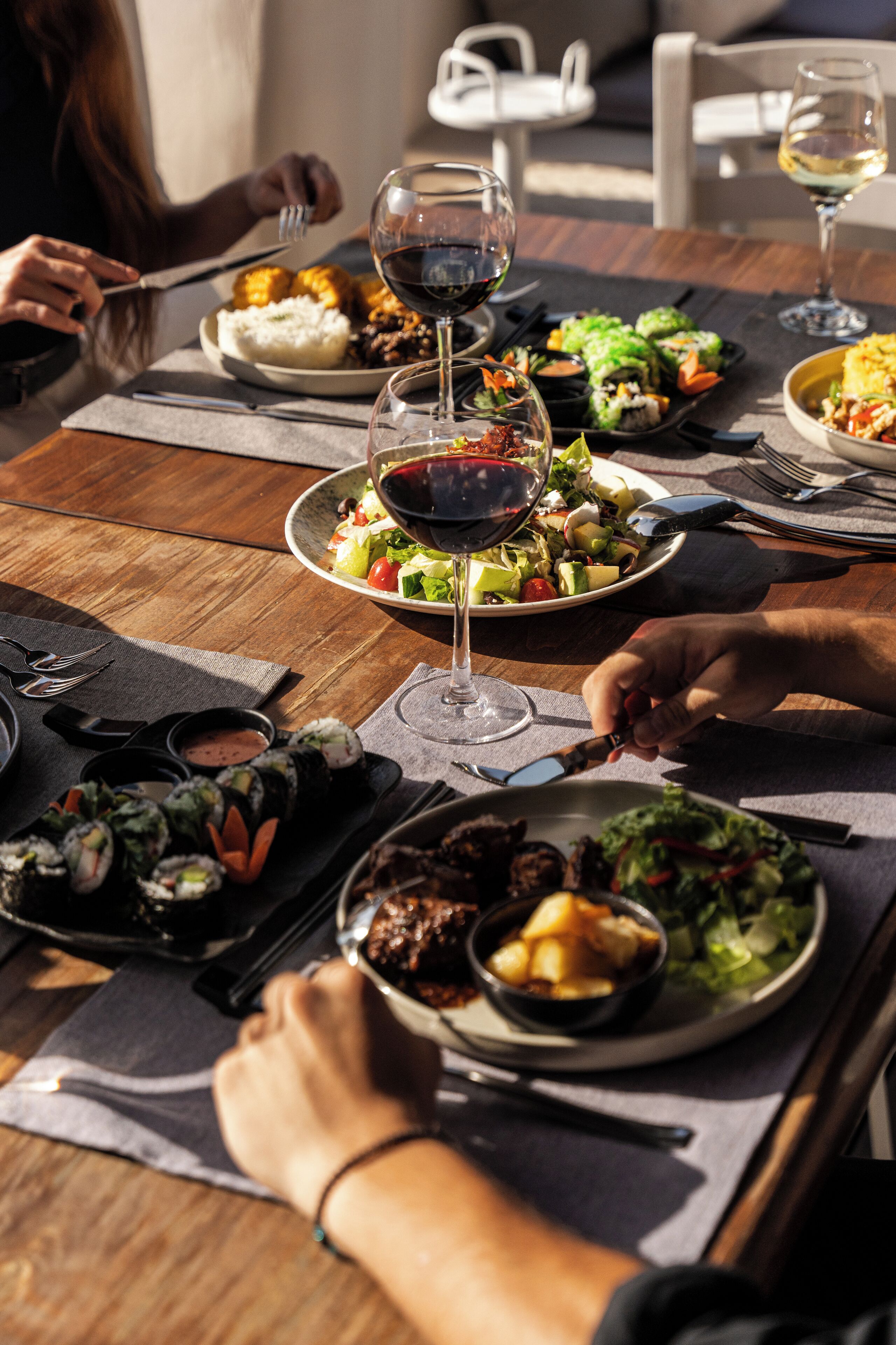 Una taula amb diversos plats, com sushi, amanides i un got de vi negre.