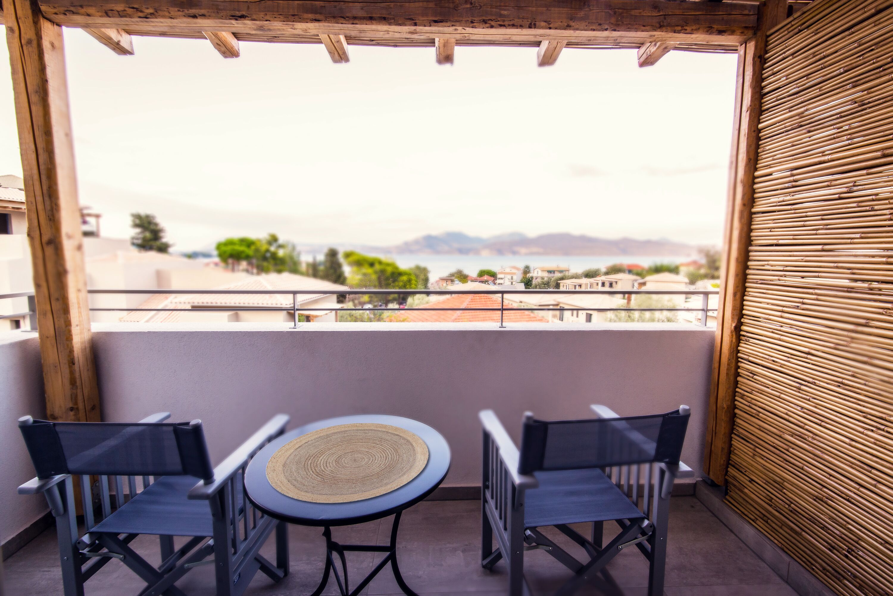 A balcony with two chairs and a table, overlooking a scenic view of a body of water and distant mountains.