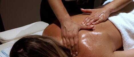 A person receiving a back massage in a room with a white bed and a white towel.