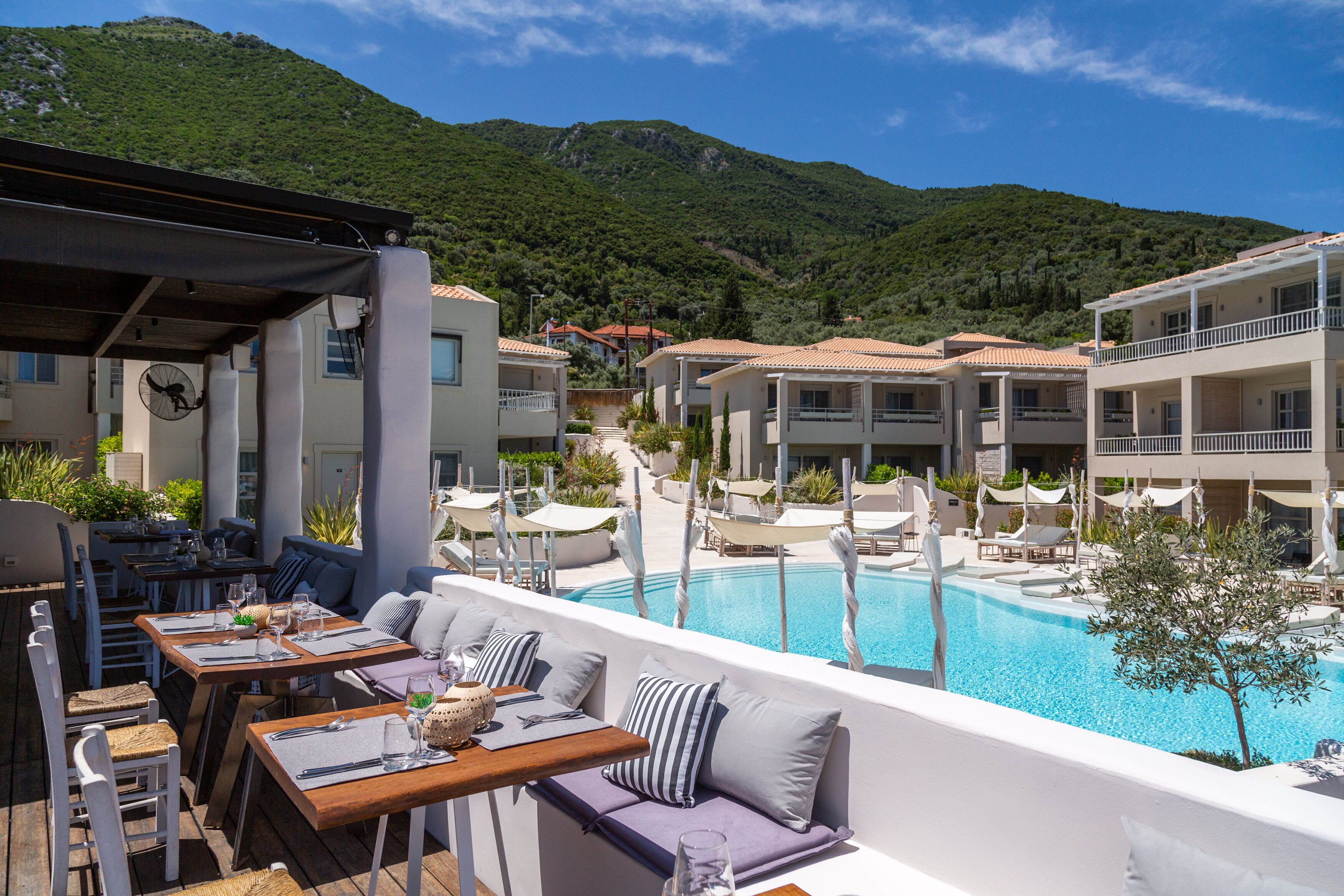Zona junto a la piscina con mobiliario exterior, una piscina y edificios al fondo.
