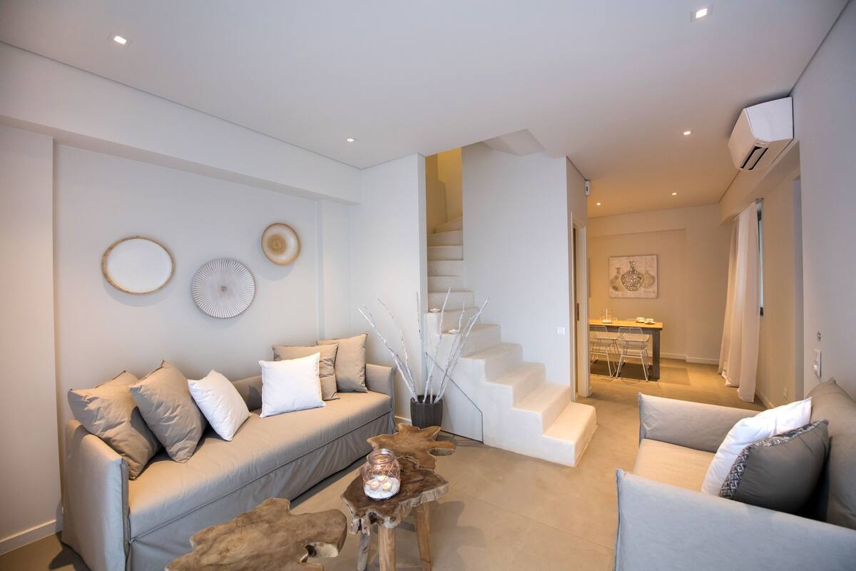 Una sala de estar moderna con un sofá, sillones, una mesa de centro y una escalera que lleva a otra habitación.