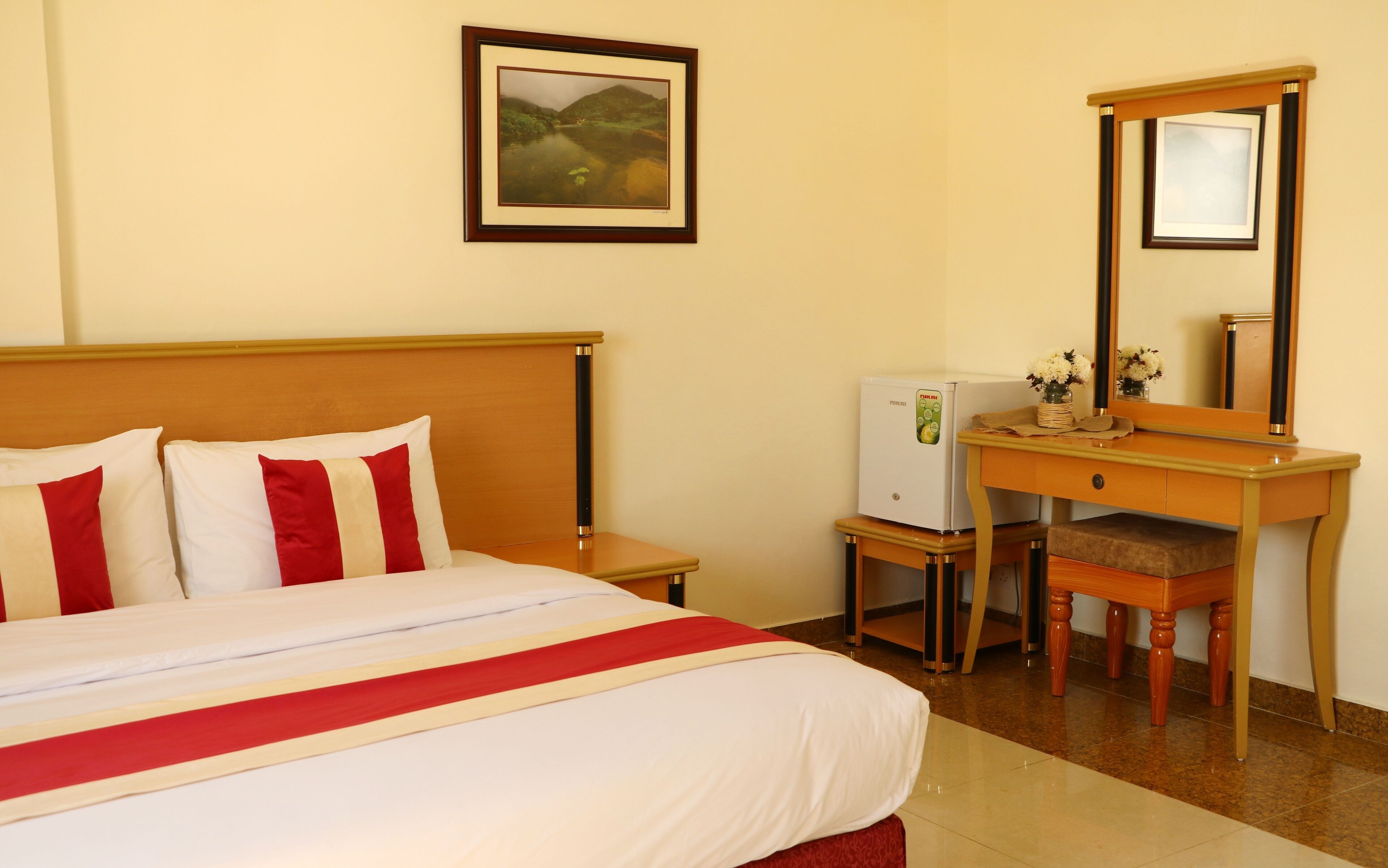 Habitación de hotel con cama, cómoda, espejo, refrigerador y un cuadro en la pared.